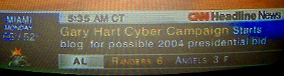 A photo from 2004 of a TV screen showing CNN, with a ticker saying "Gary Hart Cyber Campaign Starts blog for possible 2004 presidential bid"